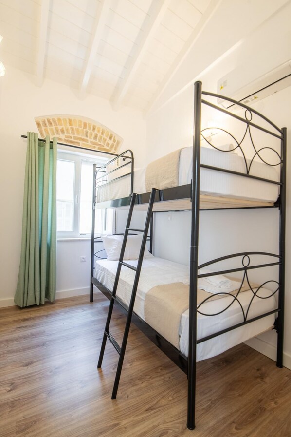A bunk bed with a ladder, a window with curtains, and wooden flooring.