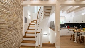 A modern kitchen with white cabinets, a wooden staircase, and a brick wall. - Casa di Marina in Corfu (Corfu)