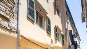 A narrow cobblestone street with a yellow building featuring a black door and green shutters. - Casa di Mana in Corfu (Corfu)