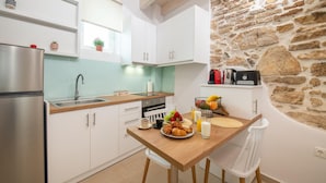 A compact kitchen with white cabinets, a stone wall, and a breakfast setup on the table. - Casa di Mana in Corfu (Corfu)