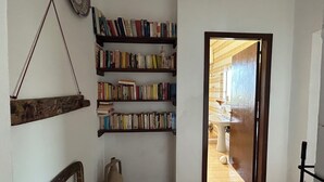 Un couloir étroit, avec une bibliothèque remplie de livres, un fauteuil rustique et une porte donnant sur une salle de bain.