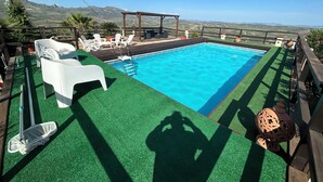 Une piscine offrant une vue sur les montagnes lointaines, entourée de chaises longues blanches et agrémentée d’une pergola.
