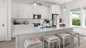 A modern kitchen with white cabinetry, a large island with bar stools, stainless steel appliances, and a view of greenery outside. - The Hive a one-minute walk to the beach! Two community pools & nearby Lagoon access (Gulf Shores)