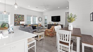 A modern living room with a white sofa, a coffee table, and a dining area with a wooden table and chairs. - The Hive a one-minute walk to the beach! Two community pools & nearby Lagoon access (Gulf Shores)