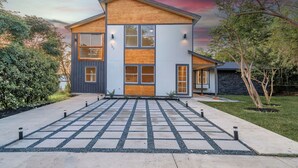 A modern two-story house with a wooden front and large windows. - Lackland AFB Luxury - Sleeps 15 · Games · Big Yard (San Antonio)