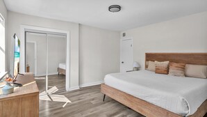 A bedroom with a wooden bed, a desk with a lamp, and a sliding door leading to a bathroom. - Lackland AFB Luxury - Sleeps 15 · Games · Big Yard (San Antonio)