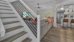 A modern kitchen with stainless steel appliances, a dining area with bar stools, and a staircase with wooden steps. - Lackland AFB Luxury - Sleeps 15 · Games · Big Yard (San Antonio)