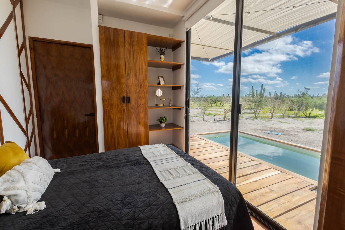 A bedroom with a large bed, wooden wardrobe, shelves, and a view of a swimming pool.