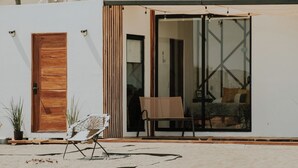 Una casa en el desierto con puerta de madera, puerta corredera de vidrio y una cama visible en el interior.