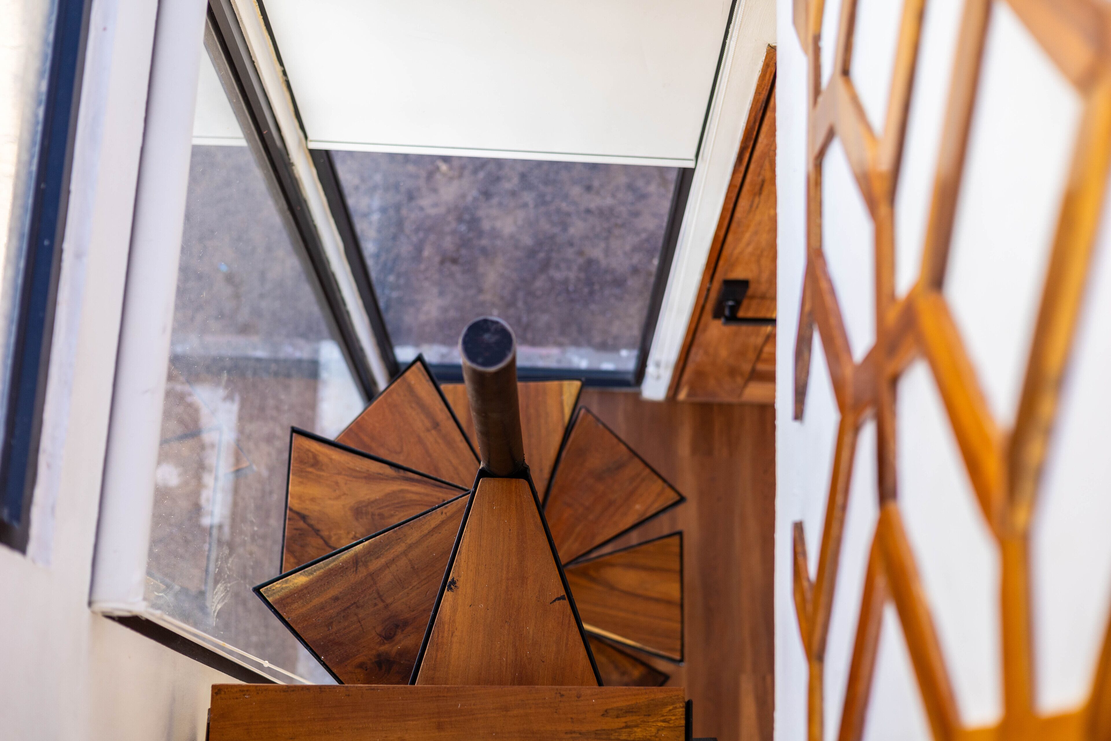 A wooden spiral staircase with a skylight above, leading to an outdoor area.