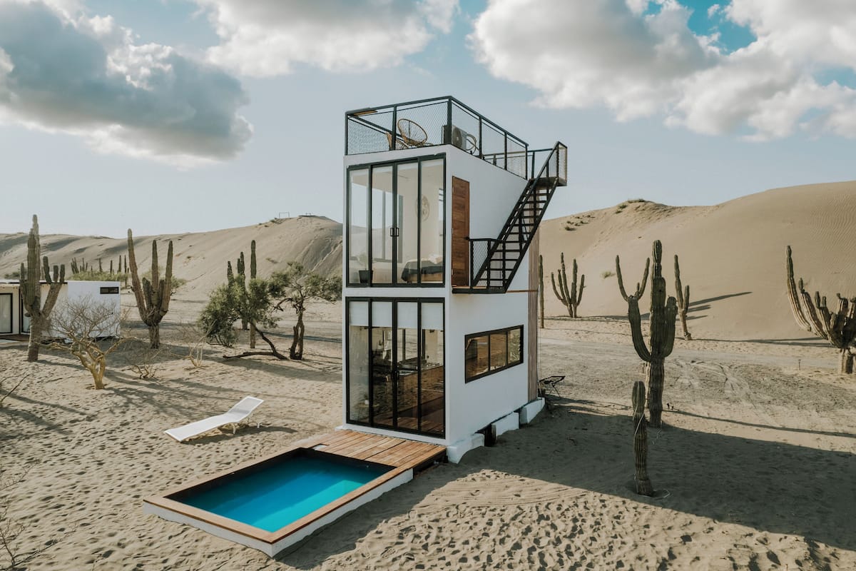 A modern, multi-level desert villa with a glass-enclosed living area, a pool, and a staircase leading to an upper deck.