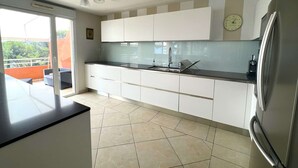 A modern kitchen with white cabinets, a black countertop, and a stainless steel refrigerator. - Apartment with air co and breathtaking sea view and direct beach access for 6 (SANARY SUR MER)