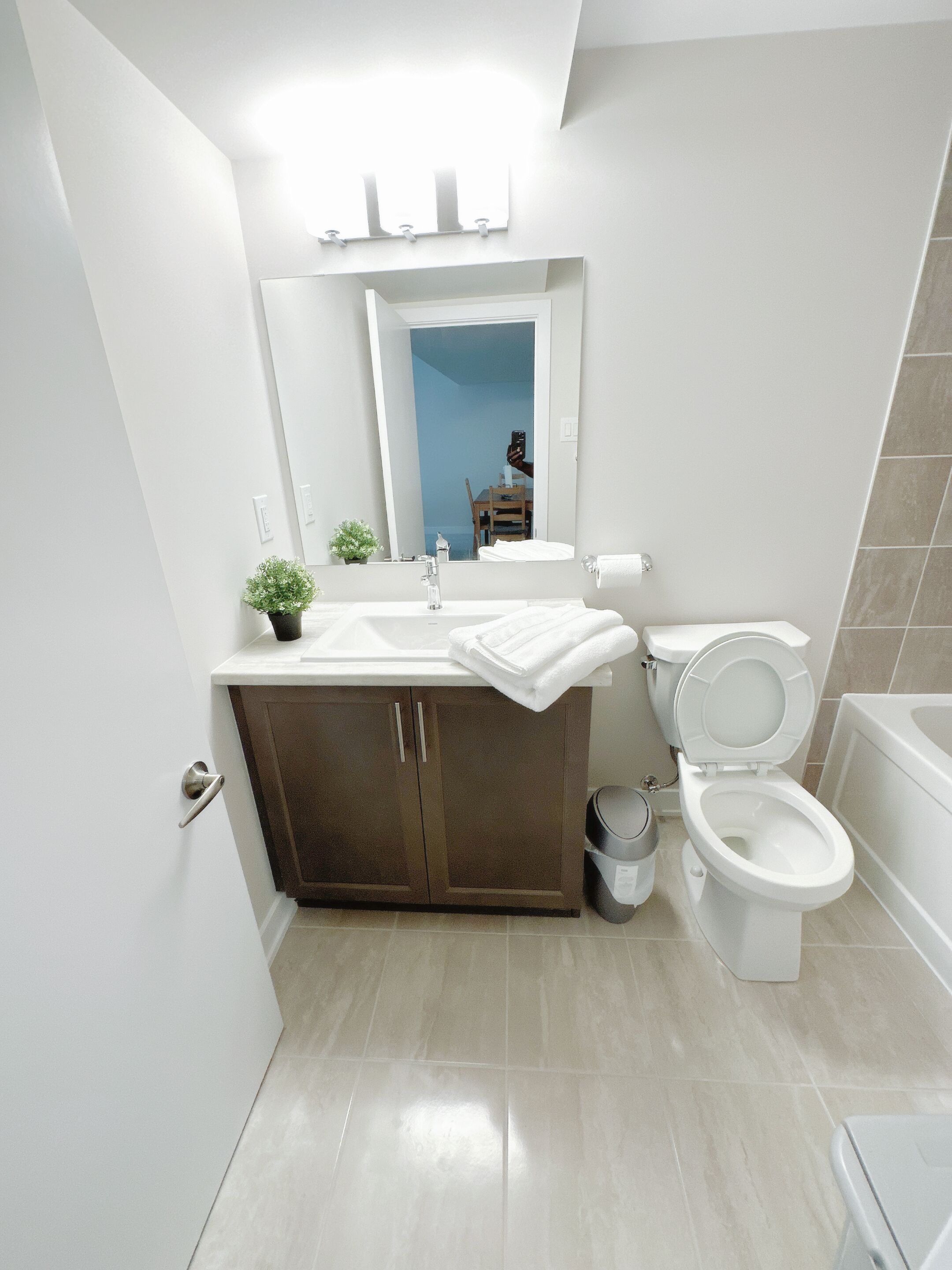 A modern bathroom with a white sink, dark wooden cabinet, white toilet, and a bathtub.