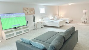 Un dormitorio moderno con una televisión grande, una cama, una mesita de noche y un ventilador de pie.