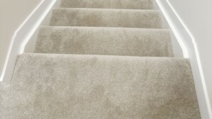 Una escalera con alfombra, paredes blancas y barandilla de madera.