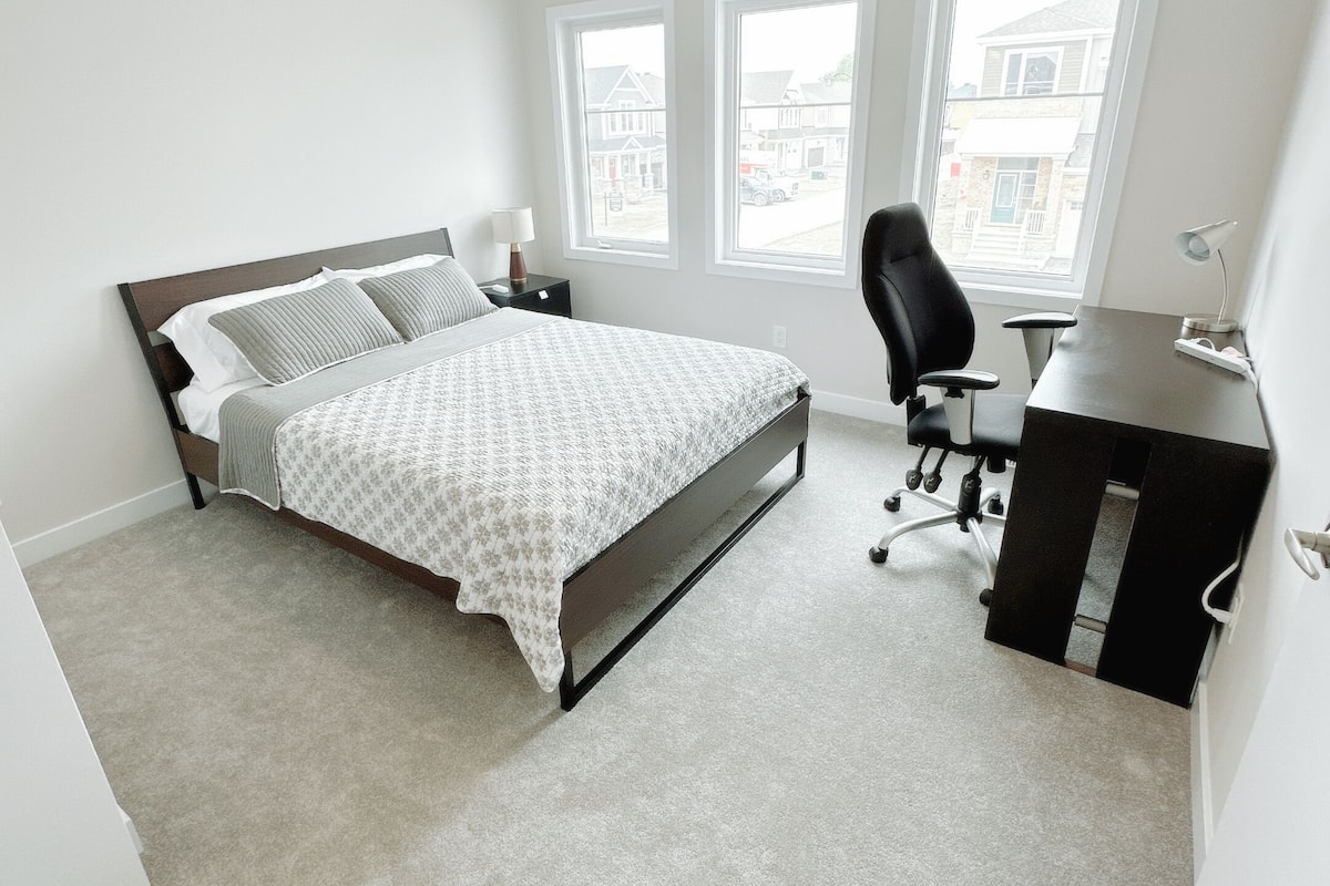 A bedroom with a bed, a desk, and two windows.