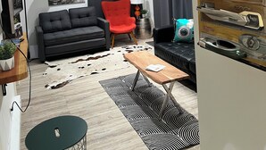 Uma sala de estar moderna com um sofá preto, uma poltrona vermelha, uma mesa de centro e um tapete estampado.