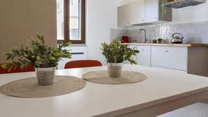 Una cucina moderna con pensili bianchi, un bollitore in acciaio inossidabile e due piante in vaso su un tavolo.