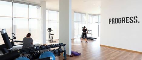A gym with exercise equipment, a woman using a treadmill, and a wall with the word 'PROGRESS.'