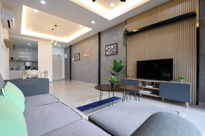 Un salon moderne avec un canapé gris, une table basse, un téléviseur et, au fond, un coin repas.