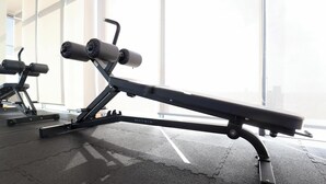 Une salle de sport équipée d’un banc de développé couché et de poids, de grandes fenêtres et d’un sol en béton.