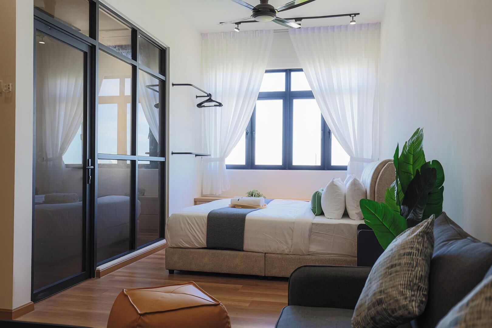 Ein modernes Schlafzimmer mit Bett, Sofa, Couchtisch und einem großen Fenster mit Vorhängen.