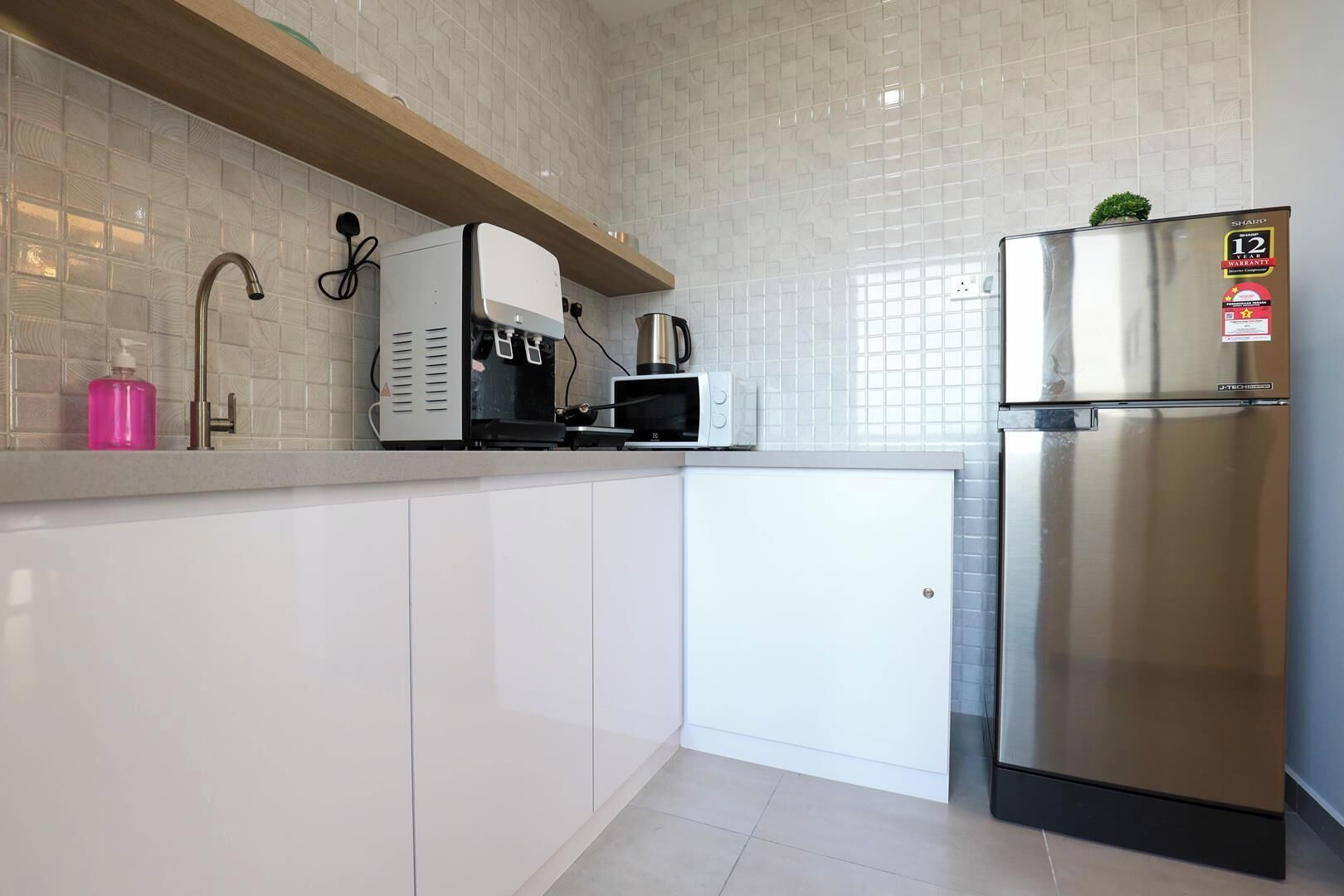 Une cuisine moderne avec des meubles blancs, un réfrigérateur en acier inoxydable, une machine à café et un four à micro-ondes.