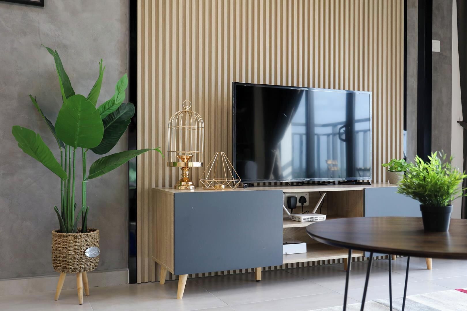 A modern living room with a flat-screen TV, a blue sofa, a round coffee table, and decorative items including a plant and a birdcage.