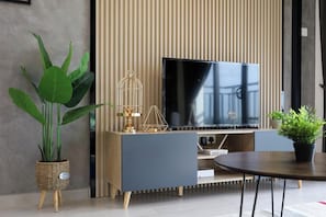 Een moderne woonkamer met een flatscreen televisie, een blauwe bank, een ronde salontafel en decoratieve objecten zoals een plant en een vogelkooi.