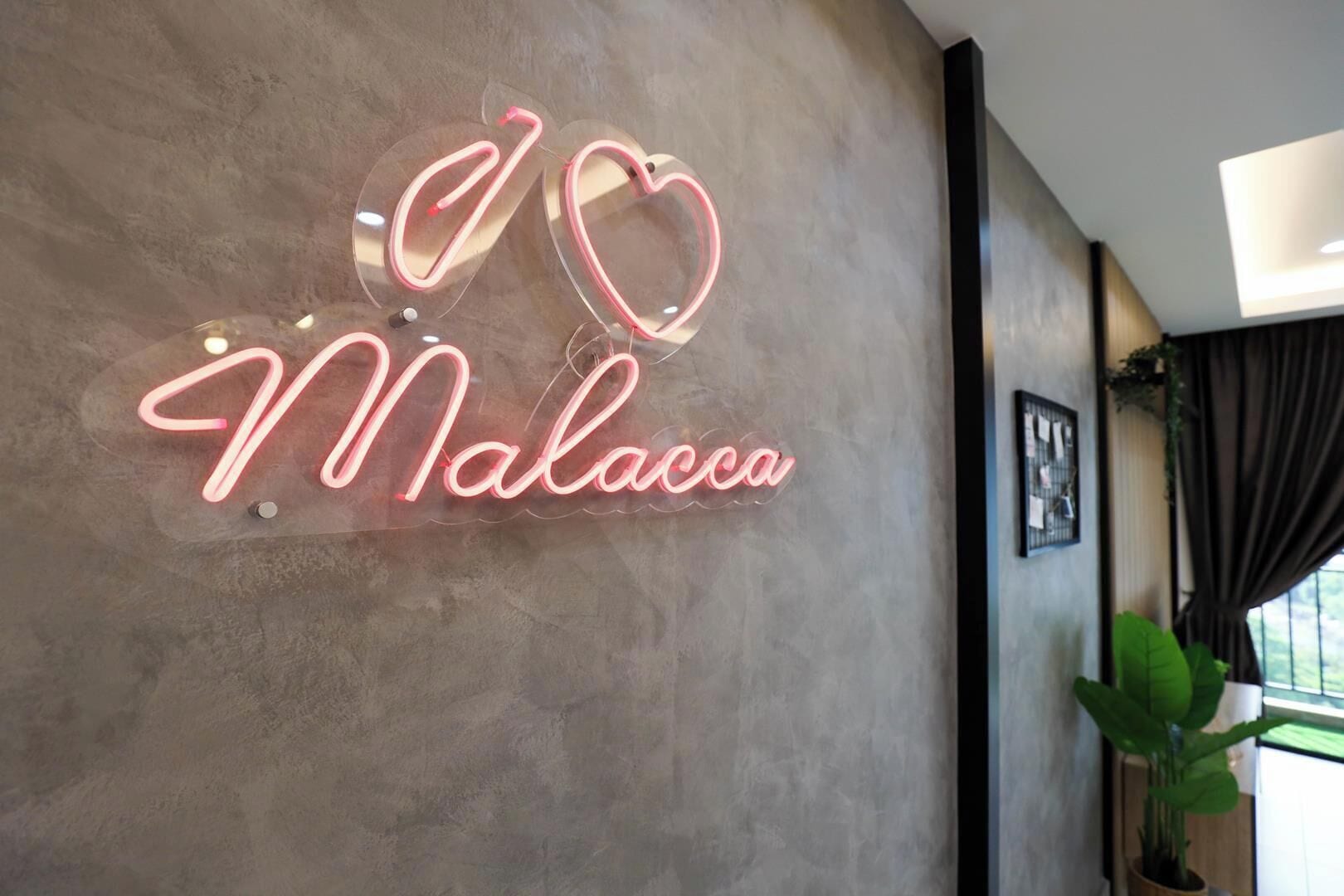 A neon sign with the text 'I ♥ Malacca' on a textured wall.
