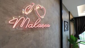 Une enseigne au néon avec le texte « I ♥ Malacca » sur un mur à texture.