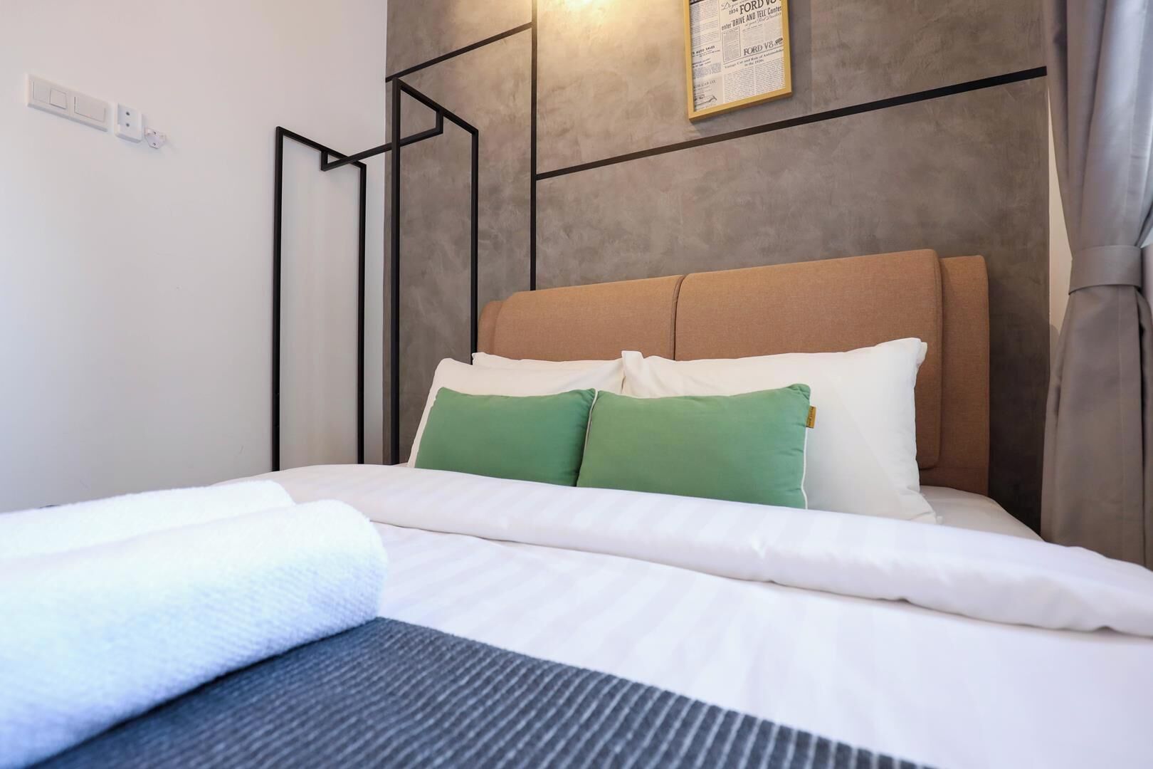 Una cama bien tendida con ropa de cama blanca y dos almohadas verdes, un cabecero con diseño geométrico y una lámpara de pared.