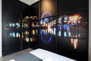 Une chambre avec un lit, une grande fenêtre qui reflète le paysage urbain et un mur offrant une vue panoramique sur la ville la nuit.