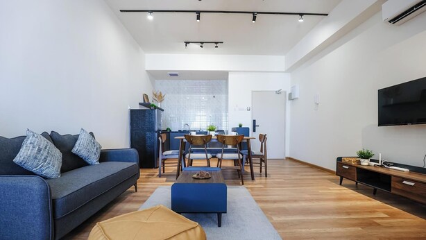 Un salon moderne comprenant un canapé, un pouf, une table à manger, des chaises et un téléviseur.
