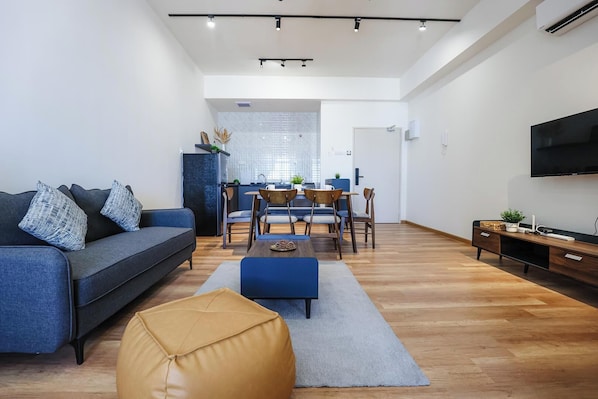 Una sala de estar moderna con un sofá, un reposapiés, una mesa de comedor, sillas y un televisor.