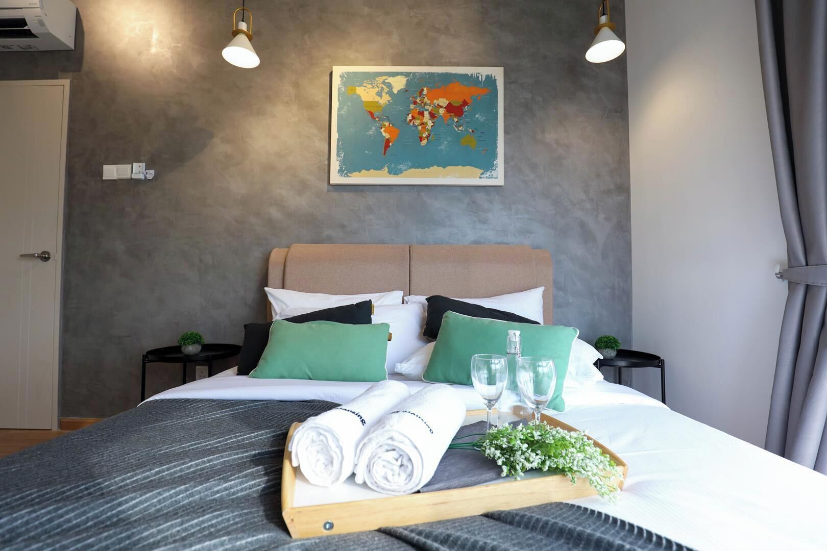 Un lit bien fait, avec des oreillers, un plateau contenant des serviettes et des verres, et une carte du monde accrochée au mur.