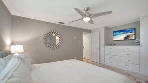 A bedroom with a bed, a ceiling fan, a TV, a dresser, and a mirror.