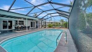 A swimming pool with a glass ceiling, surrounded by lounge chairs and a dining area.