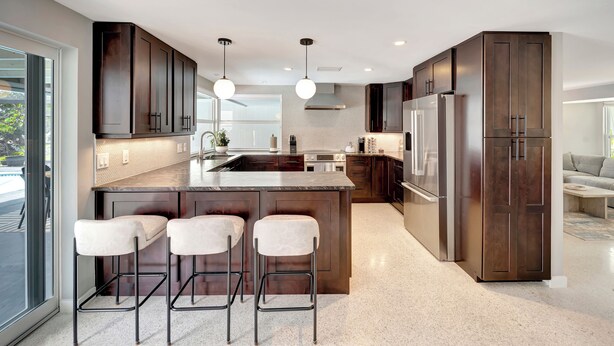 A modern kitchen with dark wood cabinets, a large island with bar stools, stainless steel appliances, and pendant lighting.