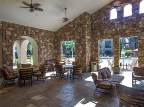 A spacious outdoor area with stone walls, multiple seating arrangements, and a view of a swimming pool.