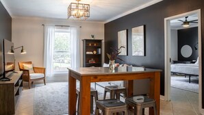 Un salón moderno con una mesa de comedor de madera, dos sillas, una estantería y un ventilador de techo.