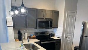 A modern kitchen with grey cabinets, a stainless steel refrigerator, a microwave, and a built-in oven. - 7550 Kirby Dr (Houston)