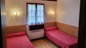 Una habitación con dos camas, una ventana con cortinas, luces fijadas a la pared y techo de madera.