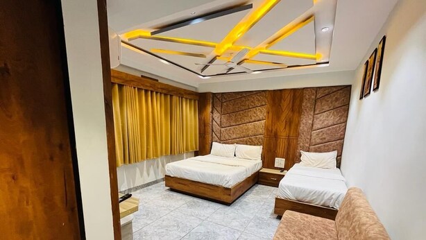 A modern bedroom with two beds, a wooden headboard, a ceiling light fixture, and a window with curtains. - Hotel Planet Villa (Ahmedabad)