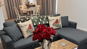 En stue med en grå sofa, et hvidt sofabord og en vase med røde blomster.