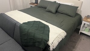 En pænt redt seng med et grønt og hvidt sengetæppe, en mørkegrå sofa og et grønt strikkegåsebord.