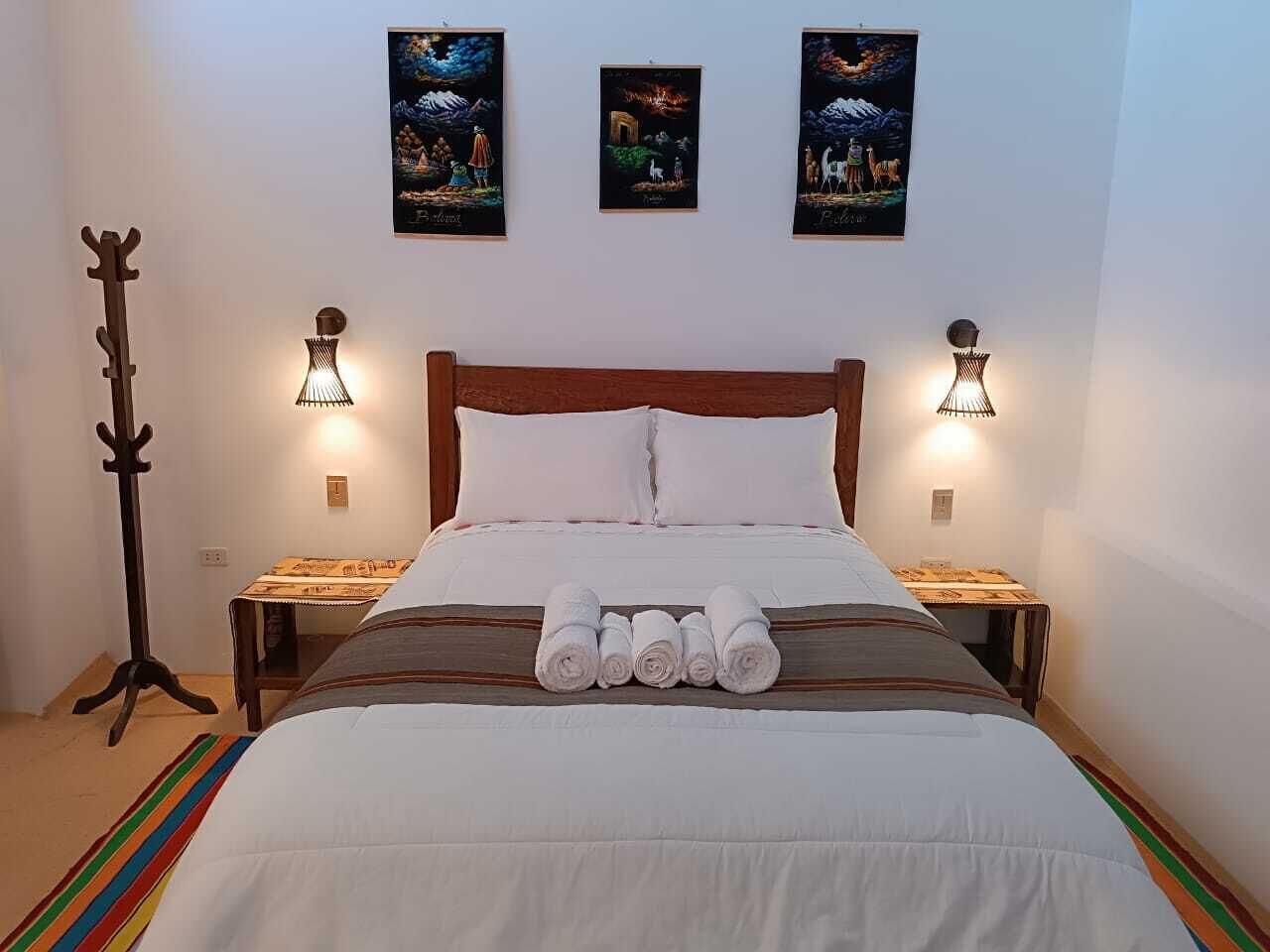 Ein ordentlich bezogenes Bett mit weißen Leinen und zusammengerollten Handtüchern, zwei Wandlampen und drei gerahmte Bilder an der Wand.