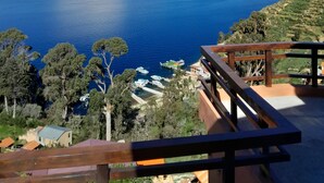 A scenic view of a coastal area with a clear blue sky, a calm sea, and a wooden deck overlooking the water. - Sol y Luna Lodge Isla del Sol Bolivia (Isla del Sol)