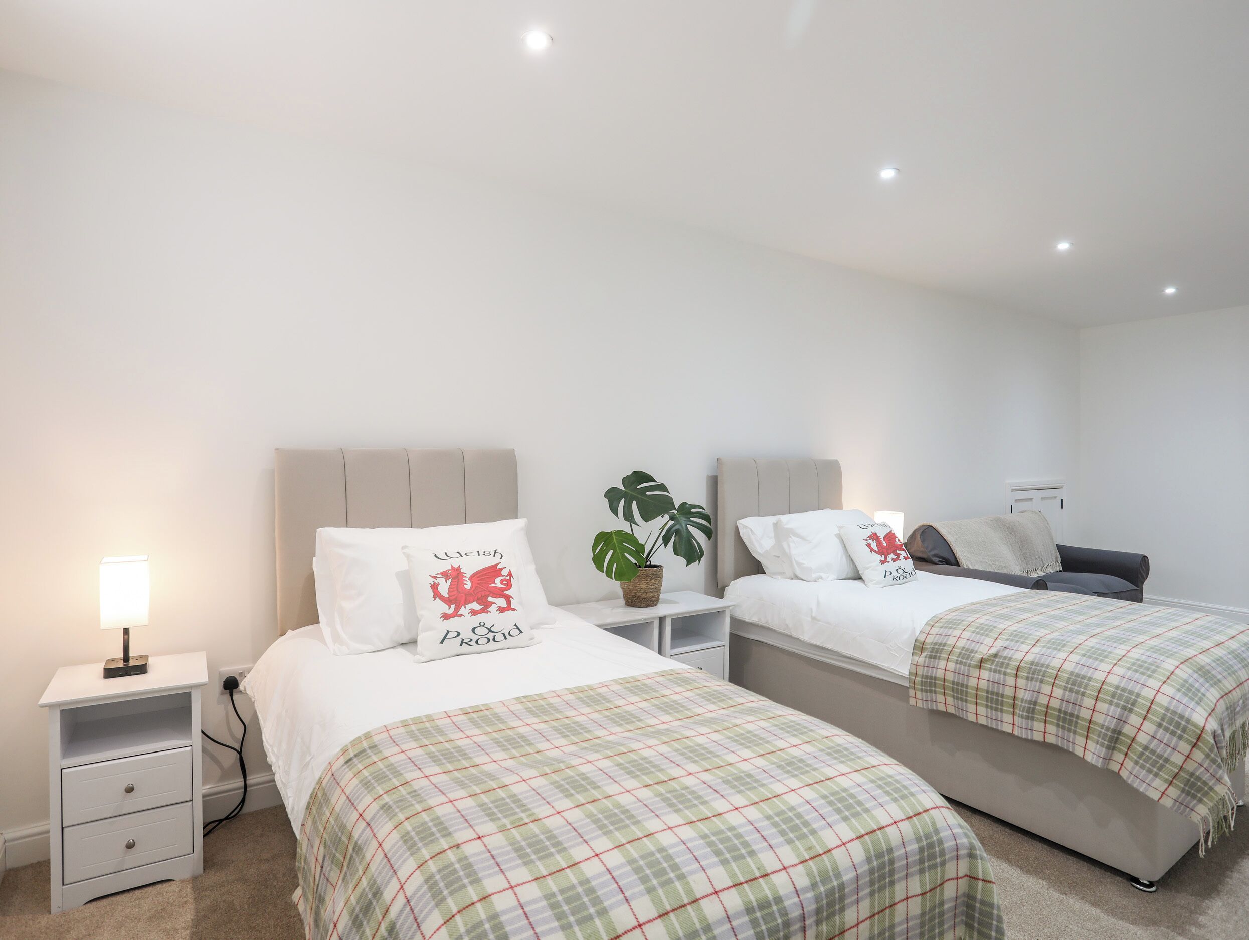 Un dormitorio con dos camas, ropa de cama blanca, una mesita de noche con una lámpara y una planta en maceta.