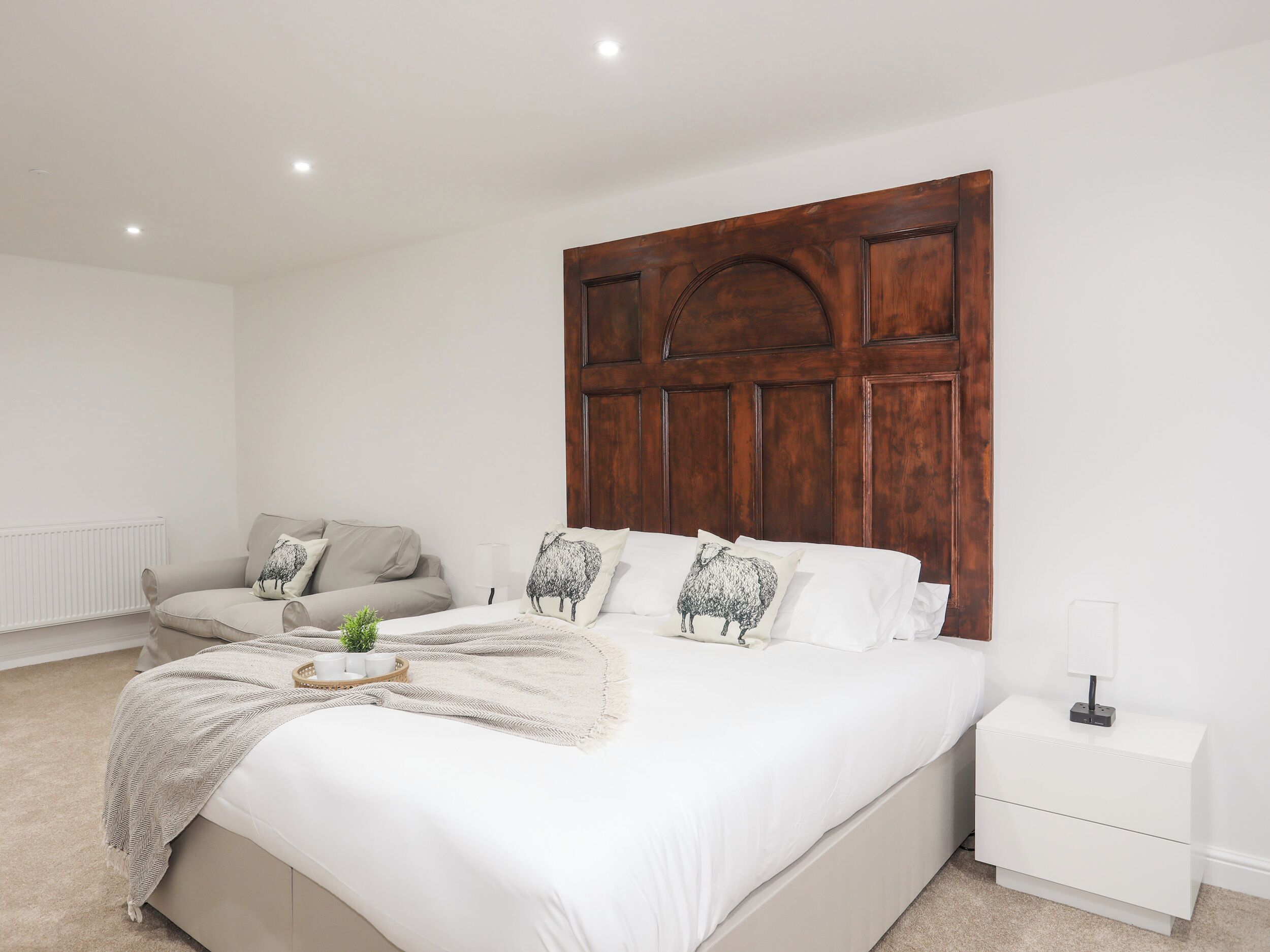Une chambre à coucher avec un grand lit, une tête de lit en bois, une table de chevet blanche et un canapé gris.